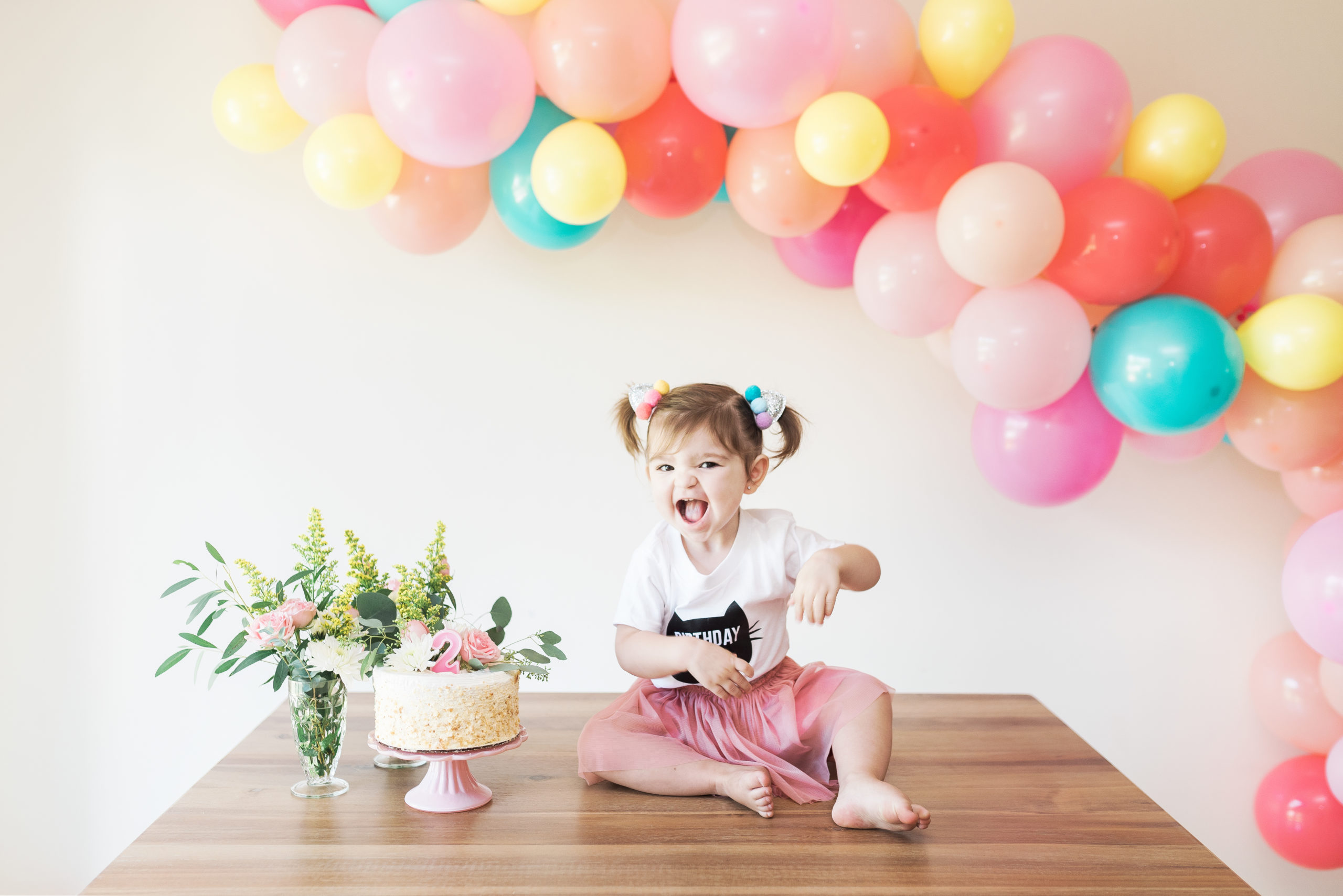 daughter next to cake and flowers with birthday balloon garland behind
