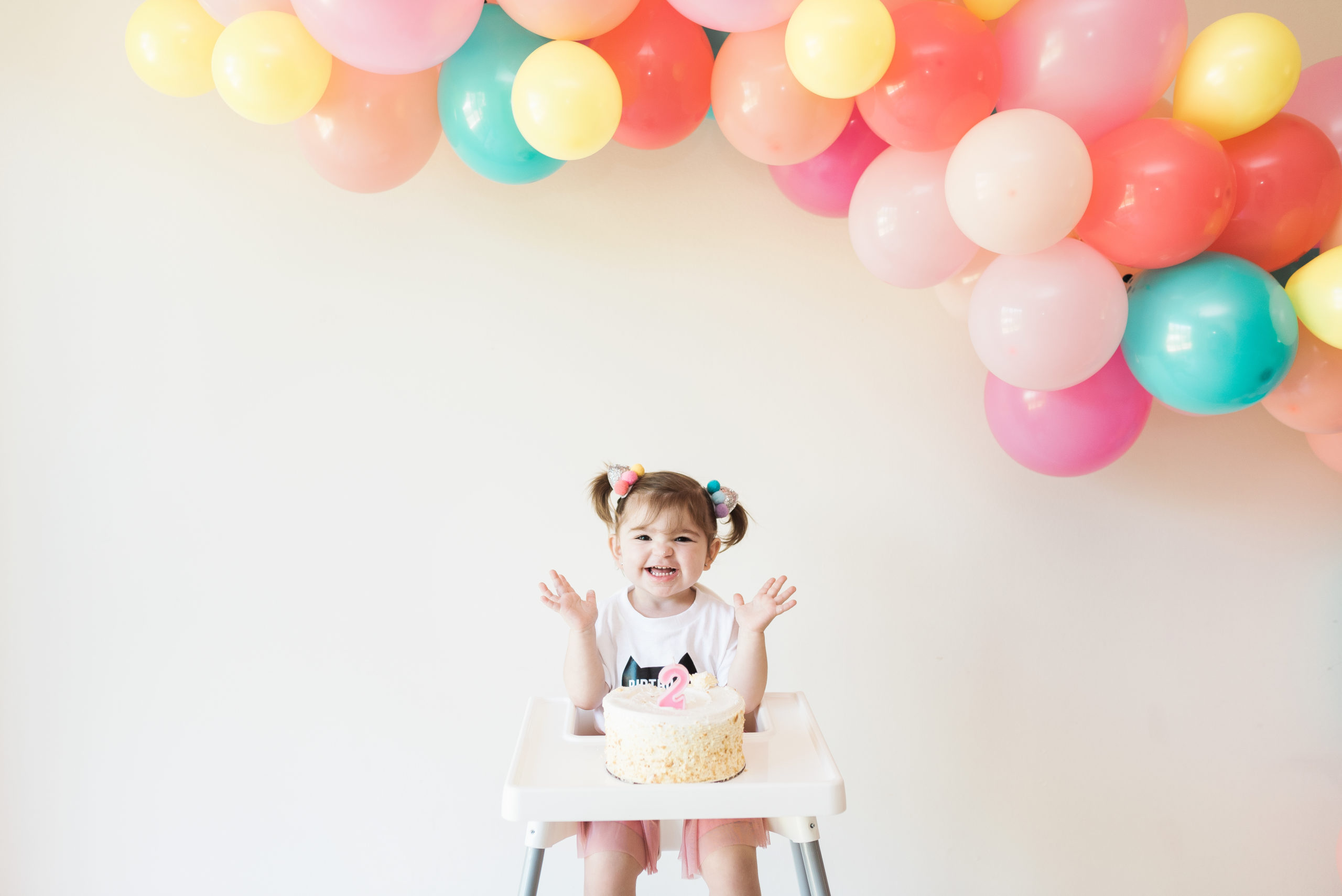 child with hands in the air smiling with birthday cake in front of her