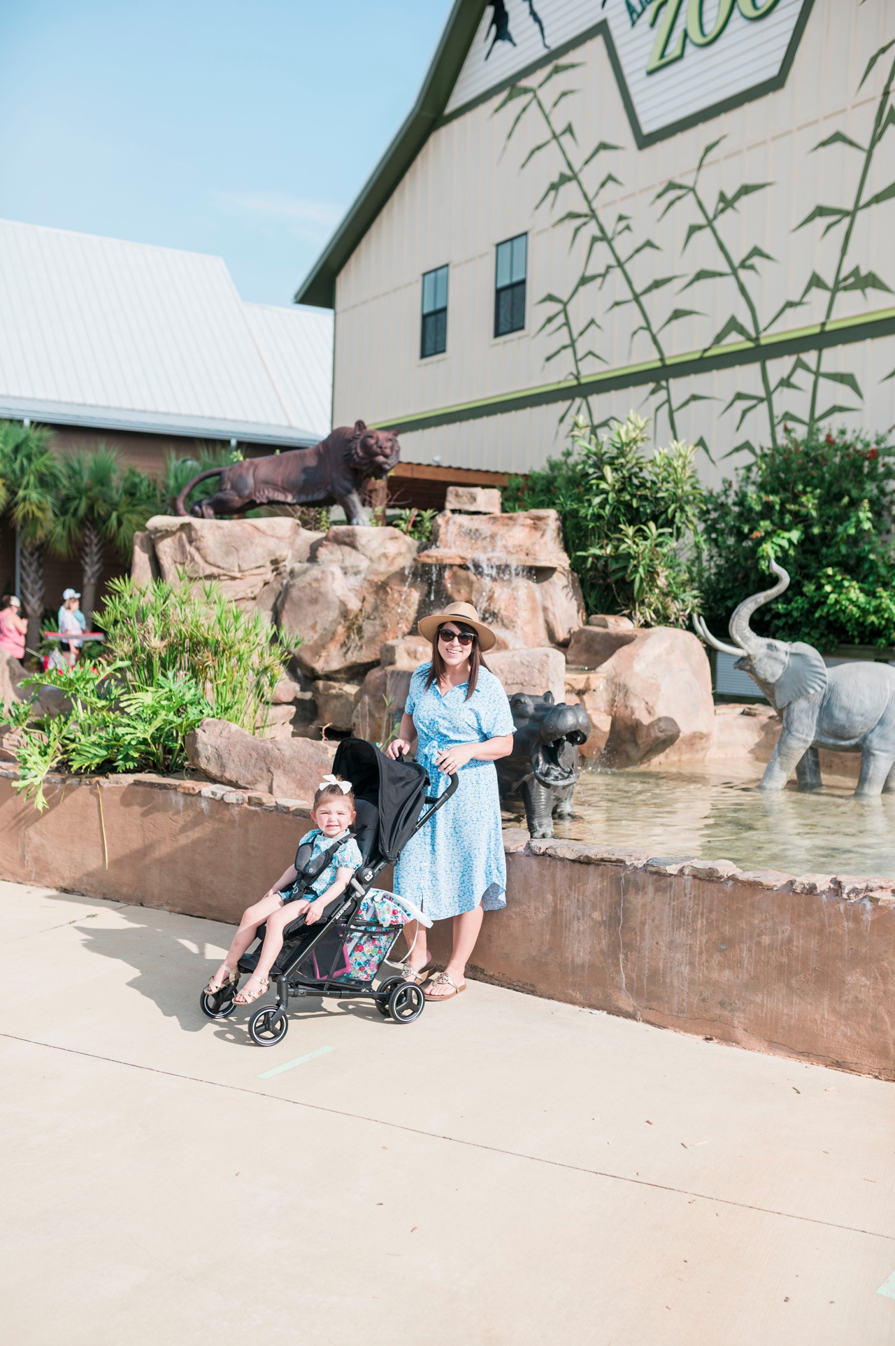 brittney naylor with stroller and daughter sitting in strolled in front of alabama gulf coast zoo sign, family vacation in gulf shores, alabama