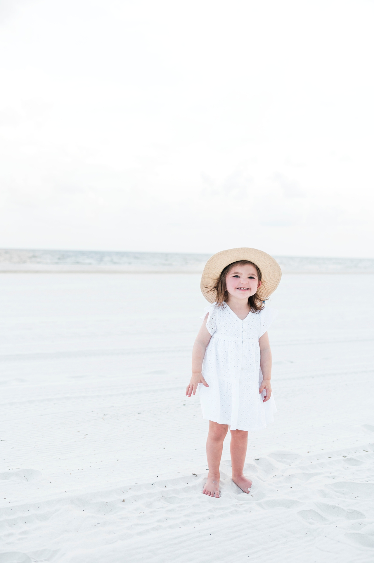 little girl in white dress and hat standing on the sand in gulf shores alabama, family vacation