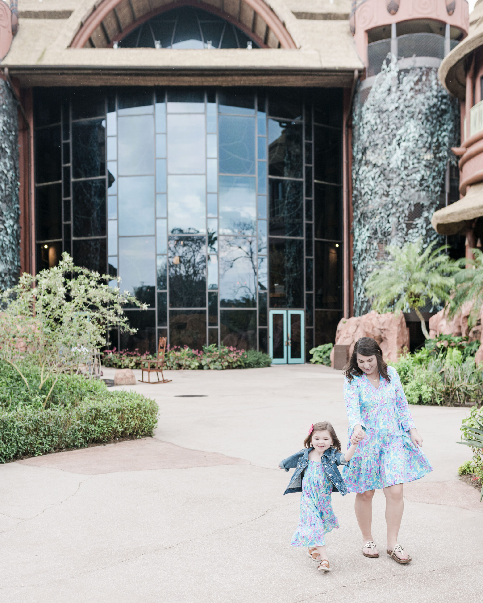 mother and daughter holding hands in matching dresses walking toward camera, animal king lodge in background dvc rentals