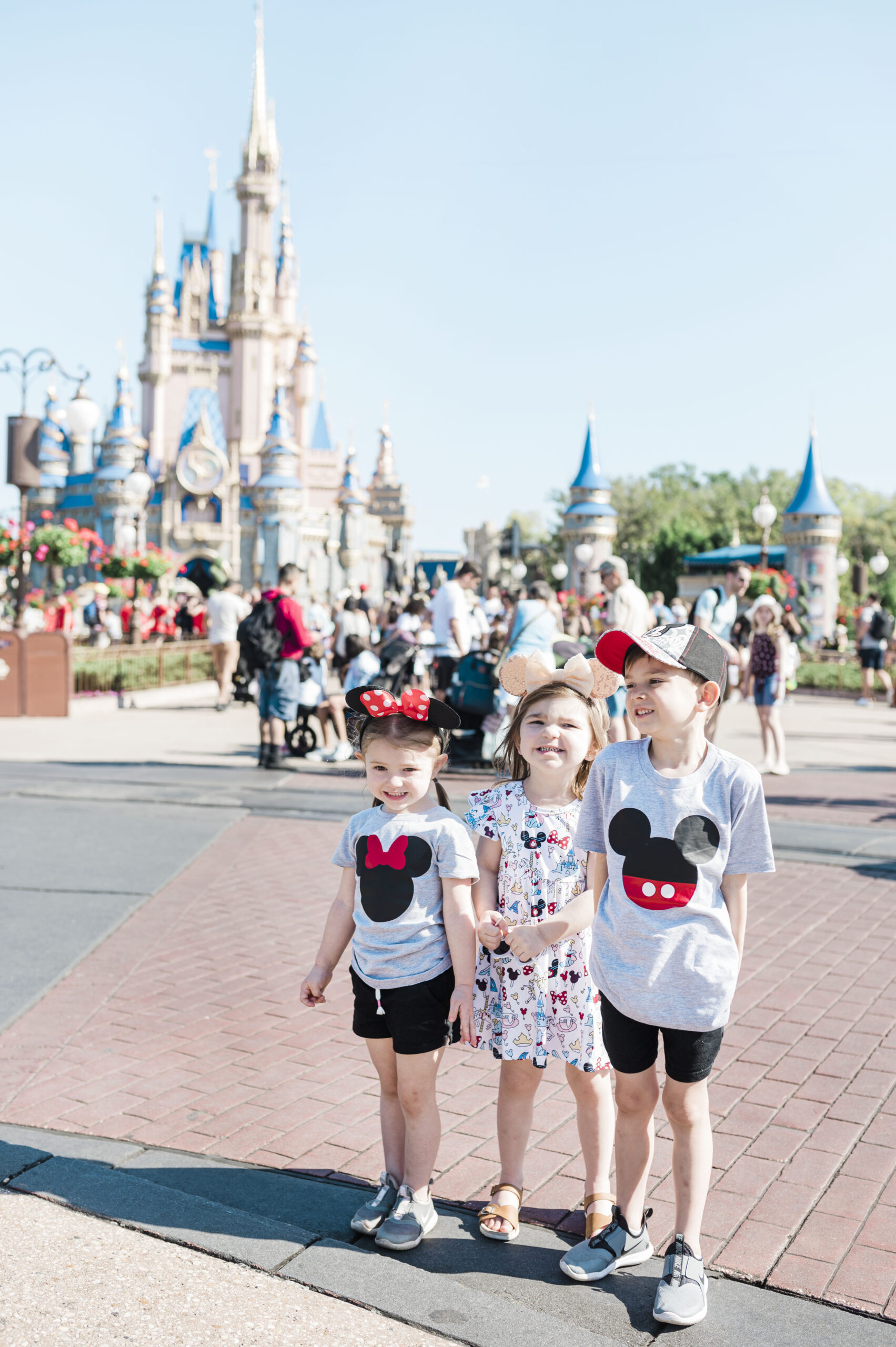 three small children which mickey mouse and standing in front of the princess castle at disney world