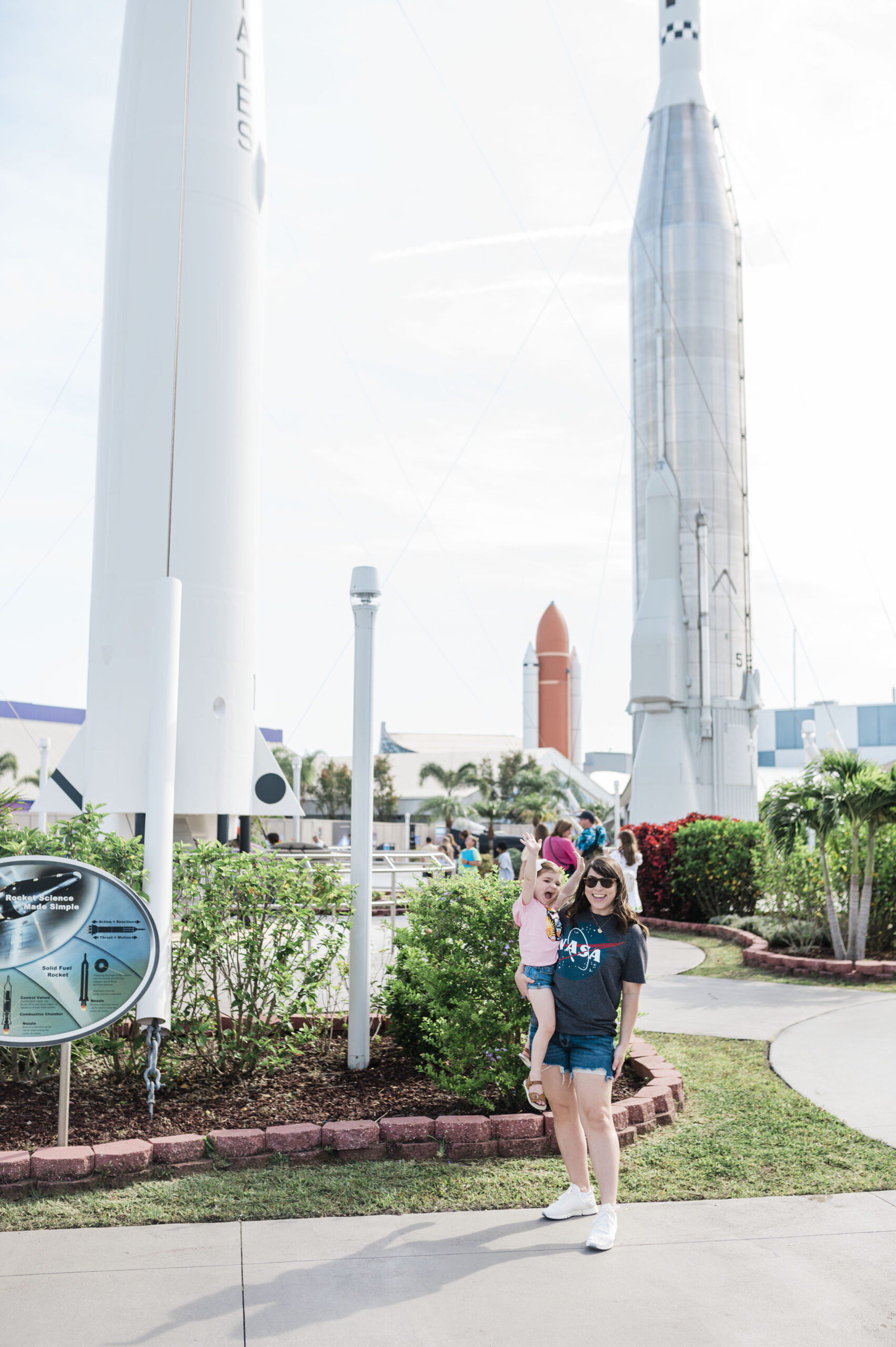 woman holding child standing in front of large rockets at the rocket garden at Kennedy Space Center in Florida