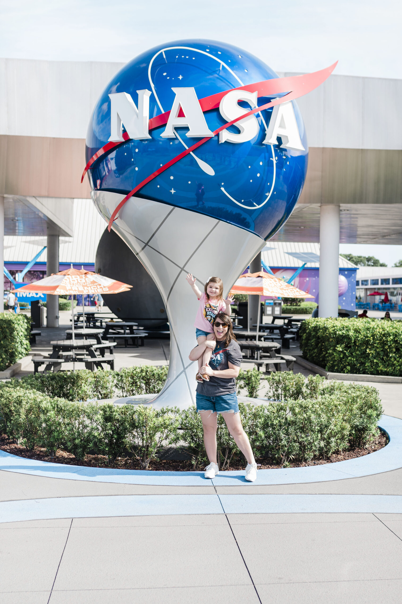 woman with child on shoulders standing in front of NASA logo