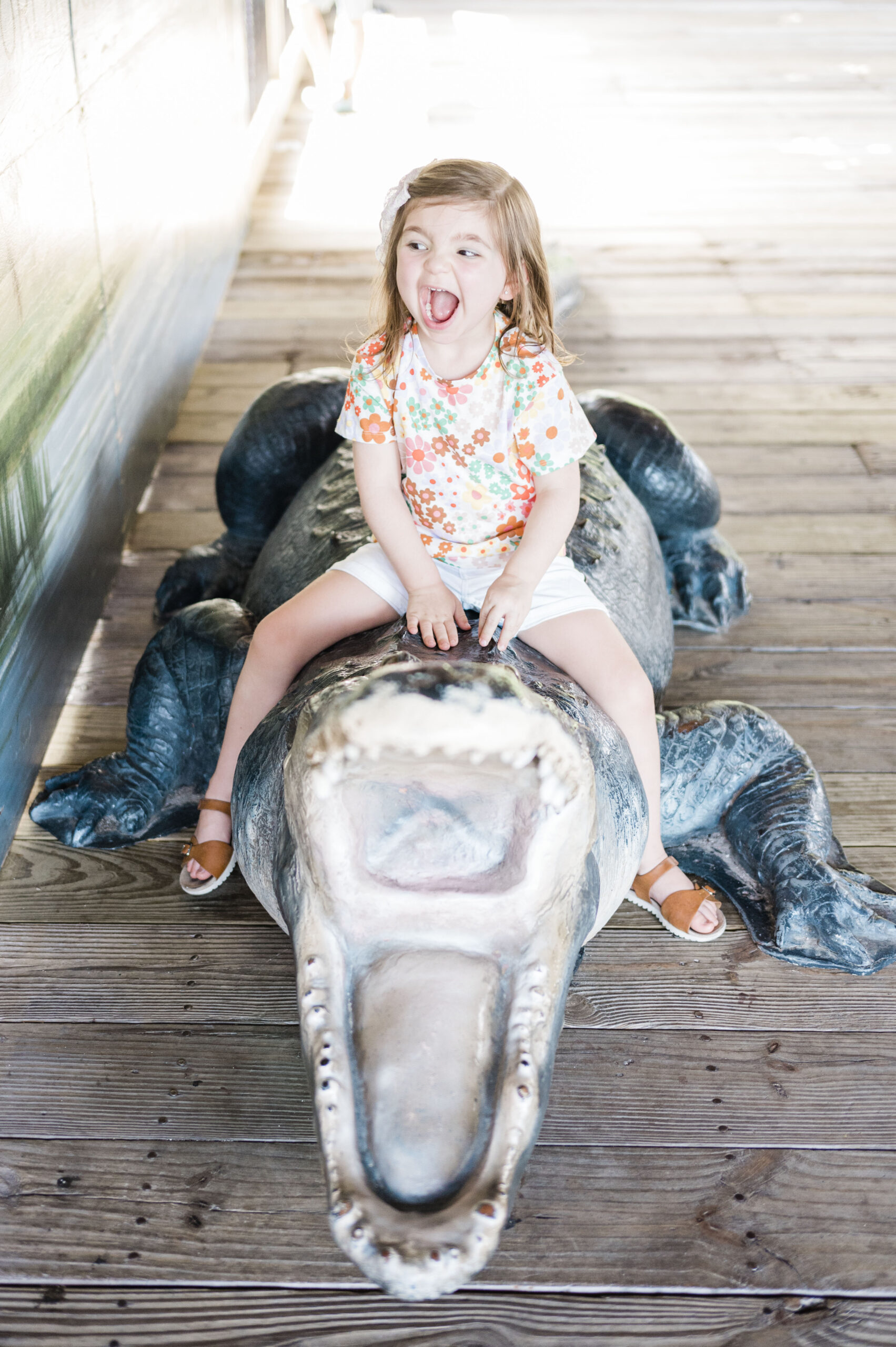 little girl with making a screaming face sitting on fake alligator