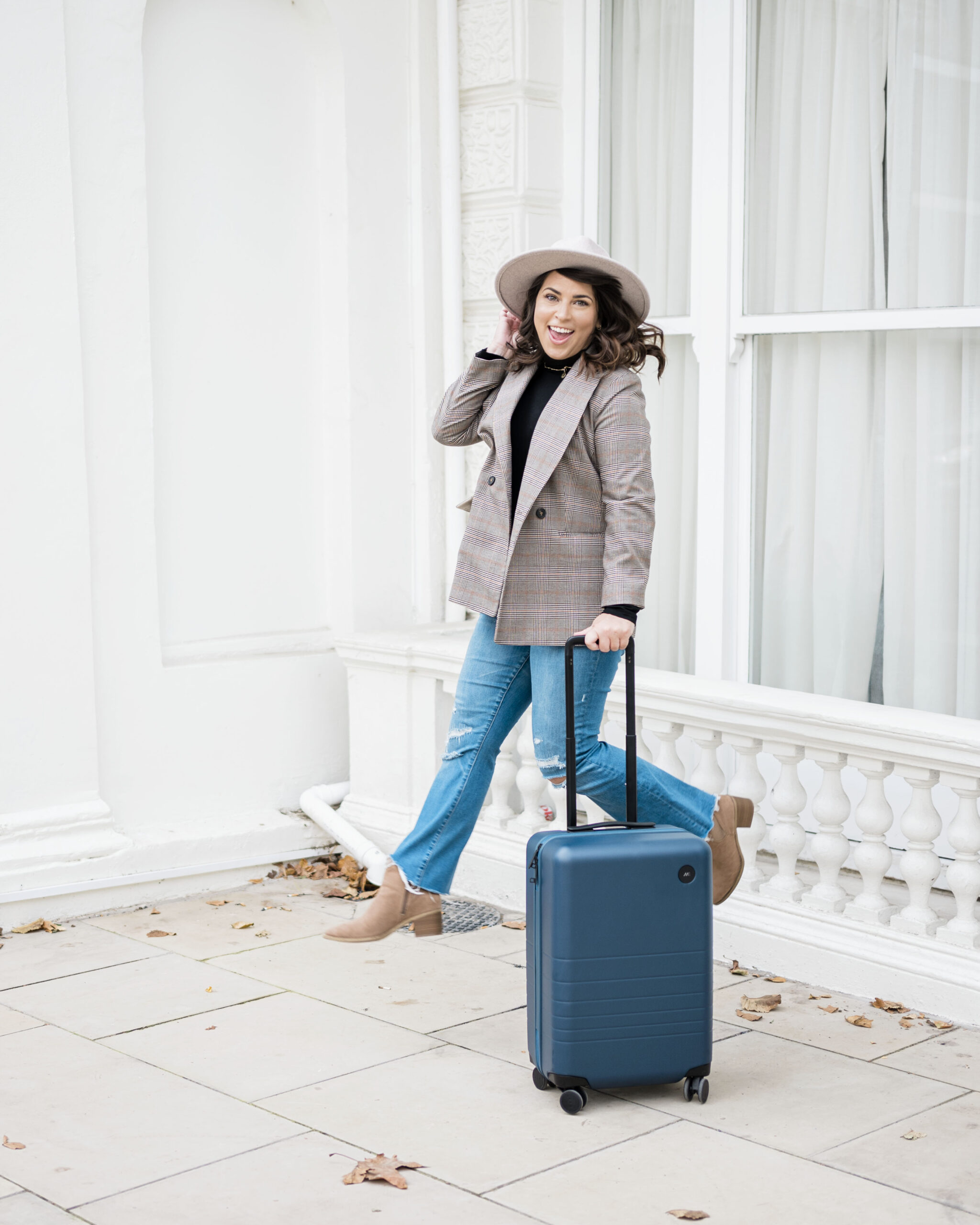 brittney naylor jumping up in the air next to a blue hardshell carryon suitcase