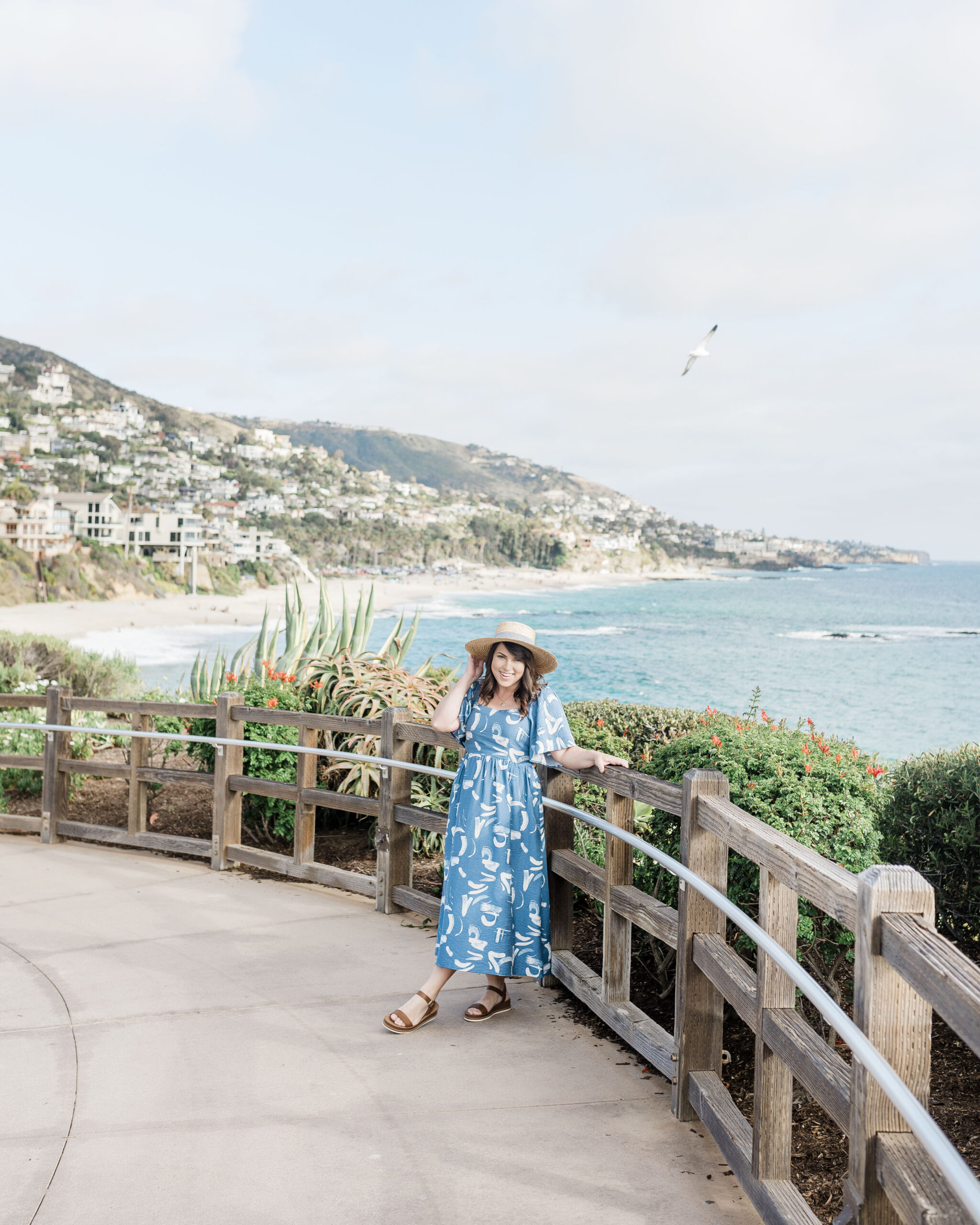 Brittney Naylor in blue maxi dress and straw hat with laguna beach coastline behind her at the Montage Resort in California