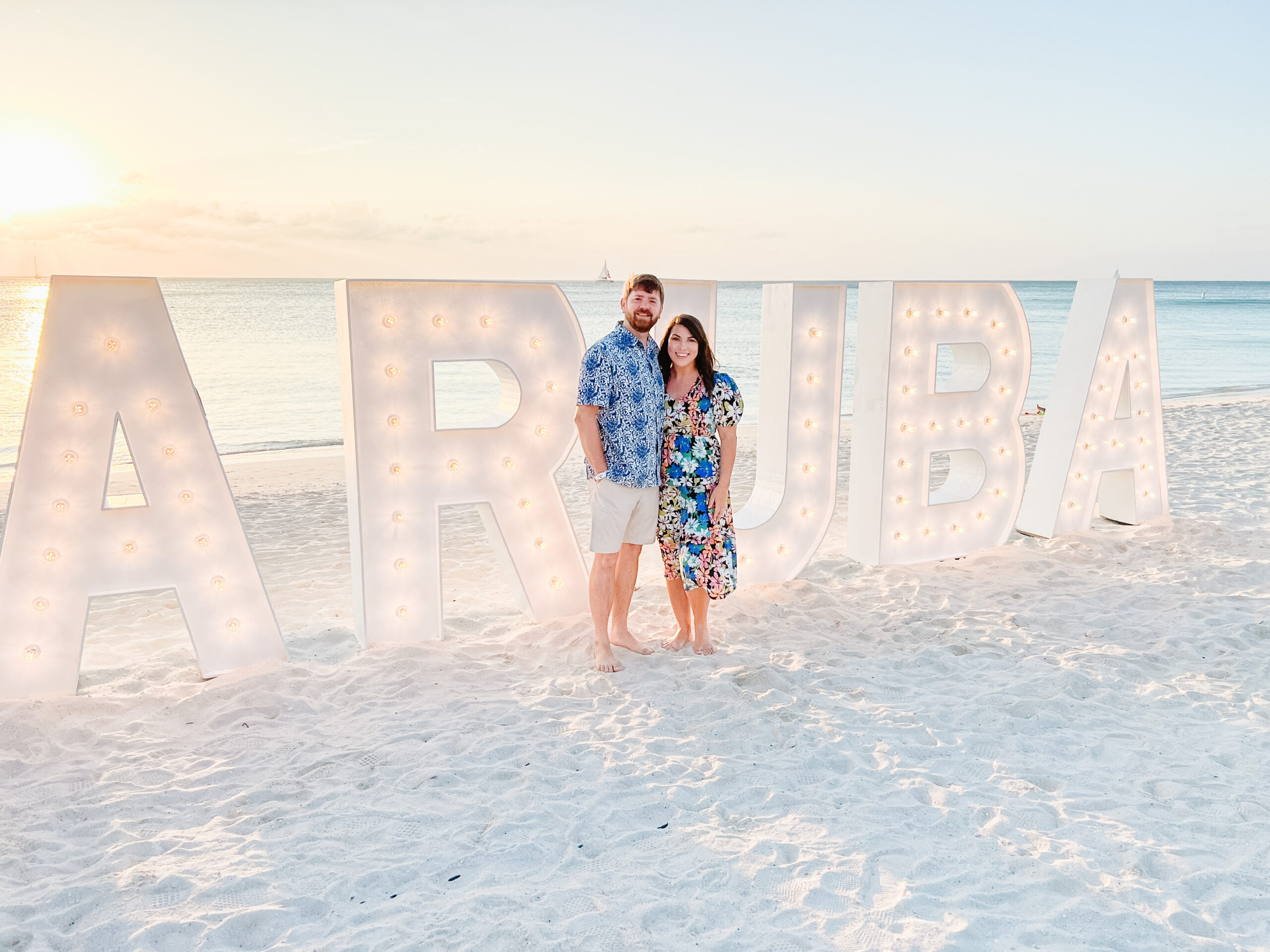 Couple standing on the beach in front of large marquee letters spelling Aruba