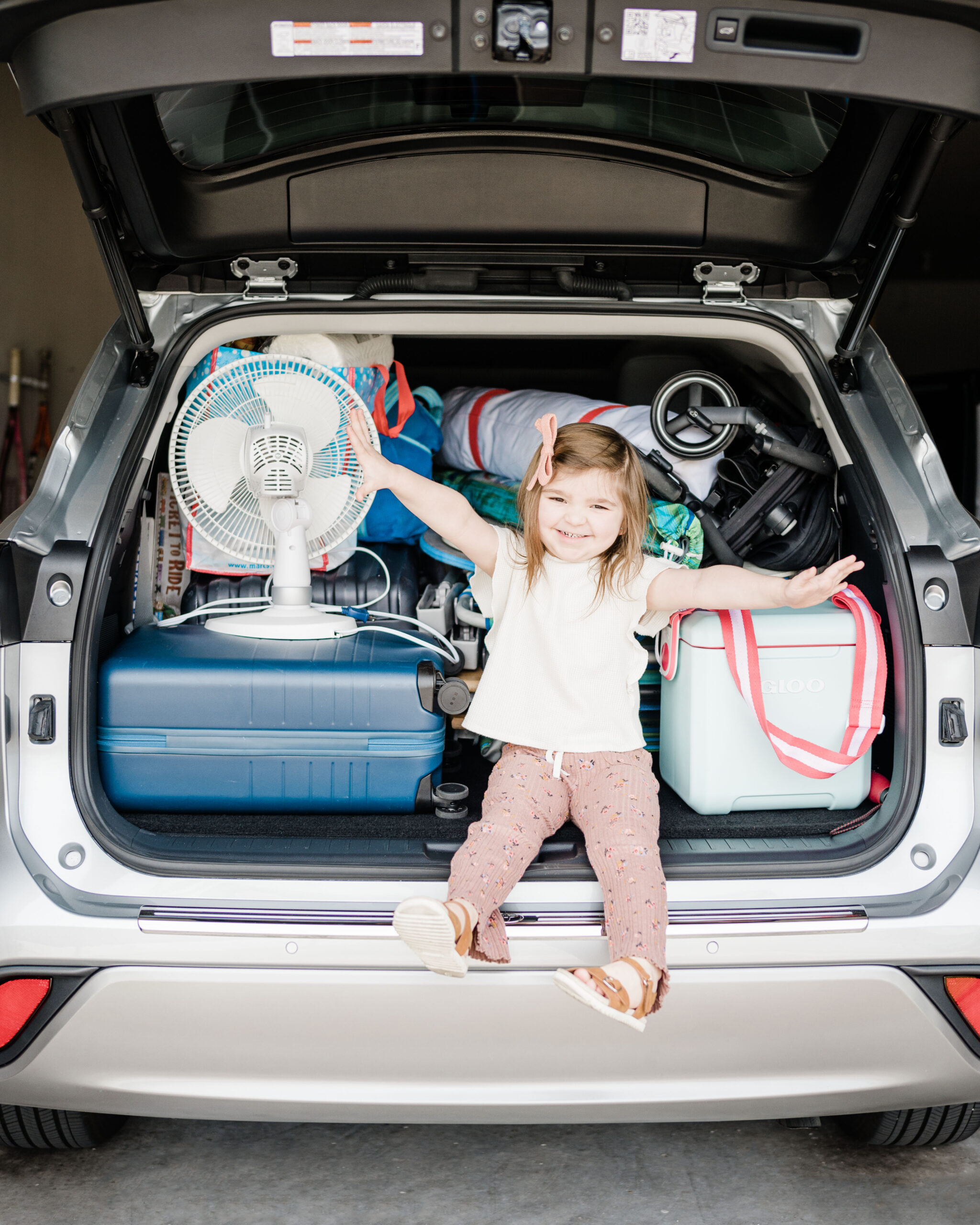 Amazon Road Trip Essentials for kids--Eleanor sitting on tailgate with luggage ready for road trip