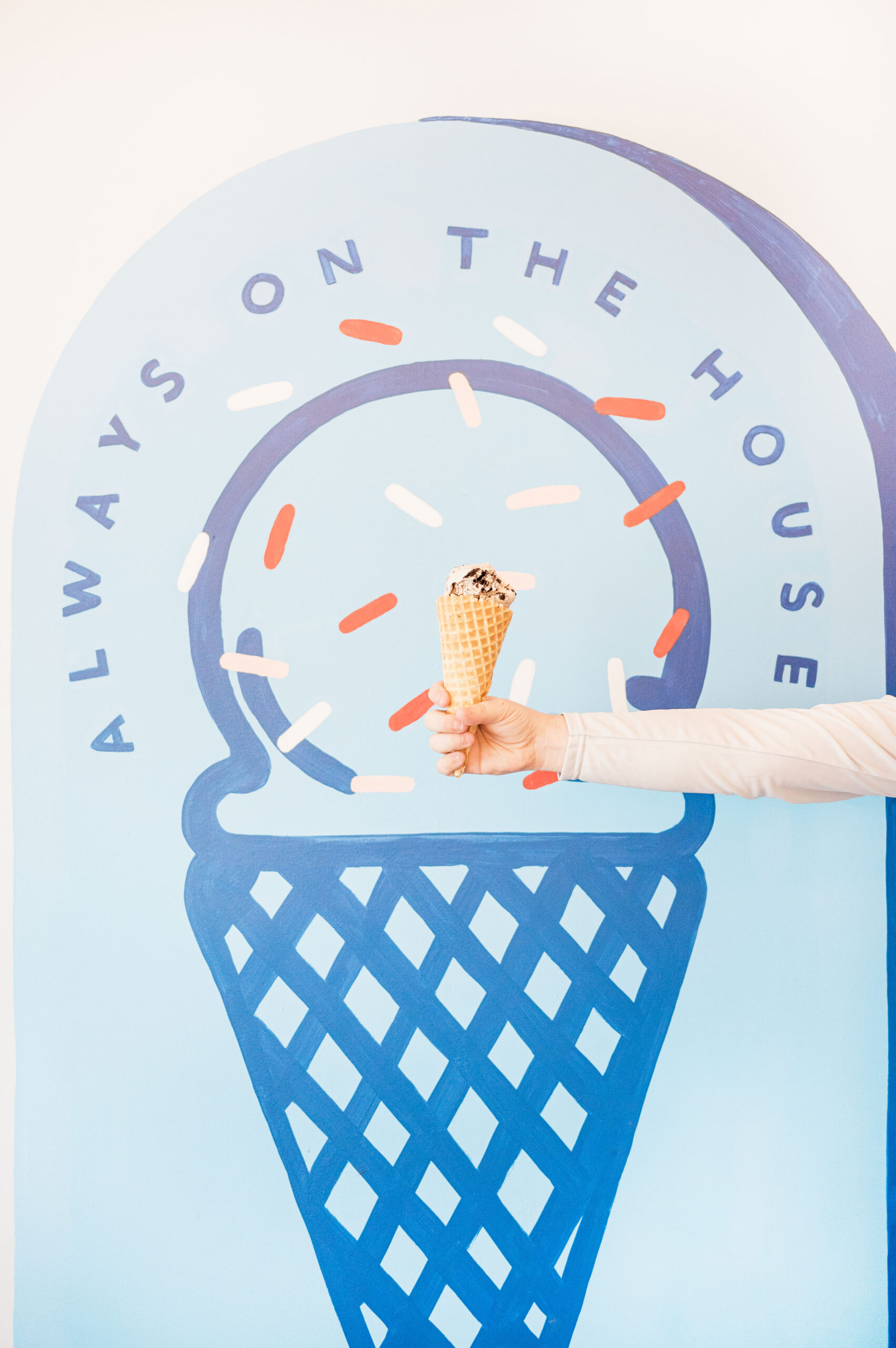 Holding ice cream waffle cone in front of blue painted cone on the wall at Mayday ice cream in Saint Augustine