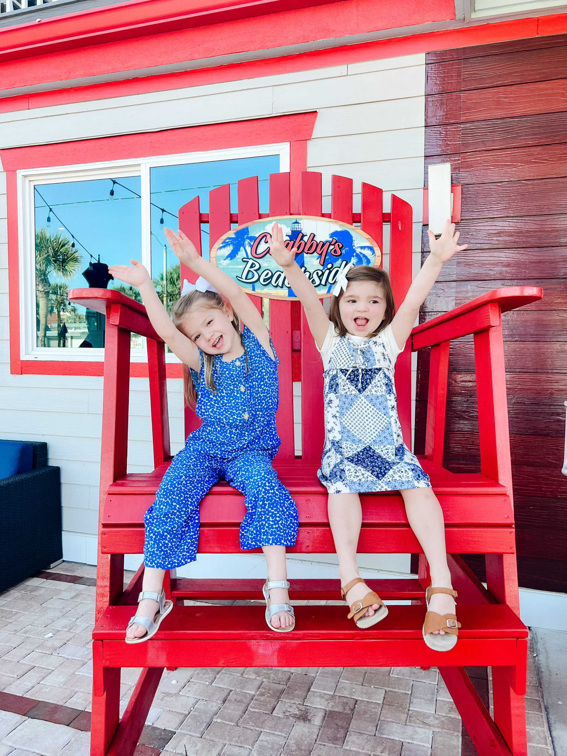 Two girls with their hands up in the air sitting in large chair outside at Crabby's Beachside in Saint Augustine