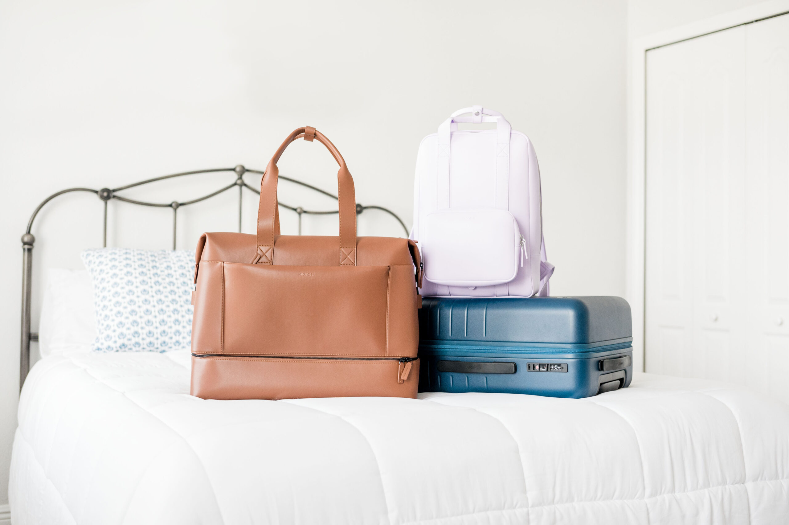 Monos luggage on bed featuring the mahogany weekender bag, backpack, and carry-on suitcase, ultimate packing list