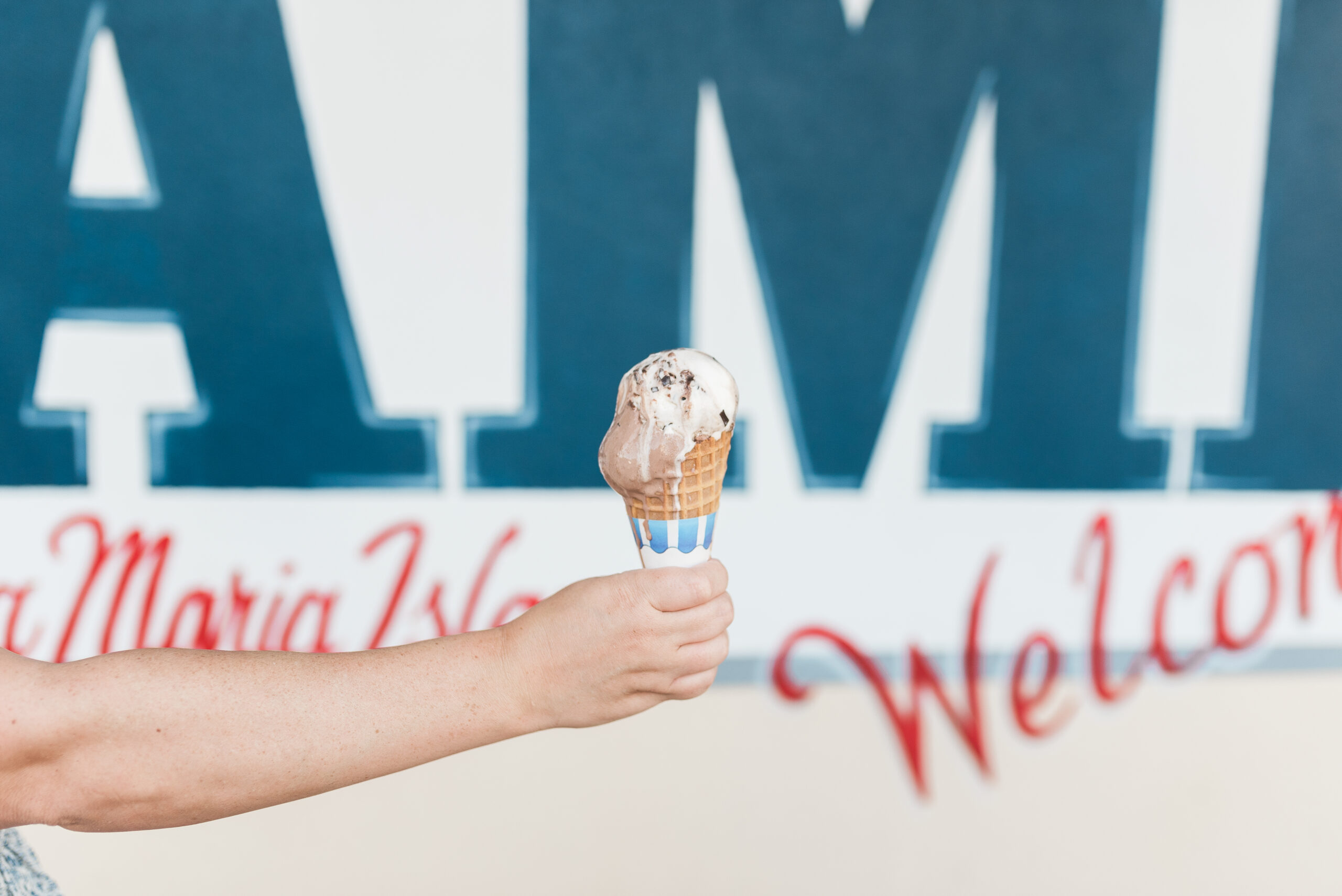 hand holding out ice cream cone in front of mural at Two Scoops in Anna Maria Island Florida