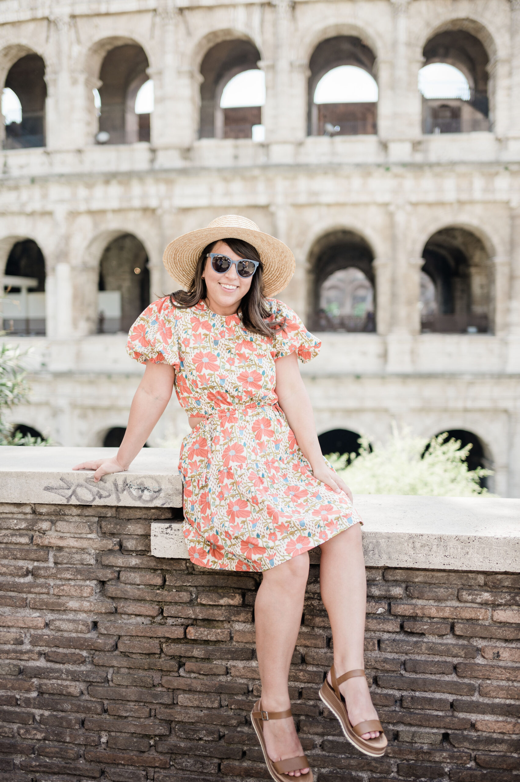Brittney Naylor wearing red floral dress sitting on wall with the Colosseum behind her. 36 Hours in Rome.