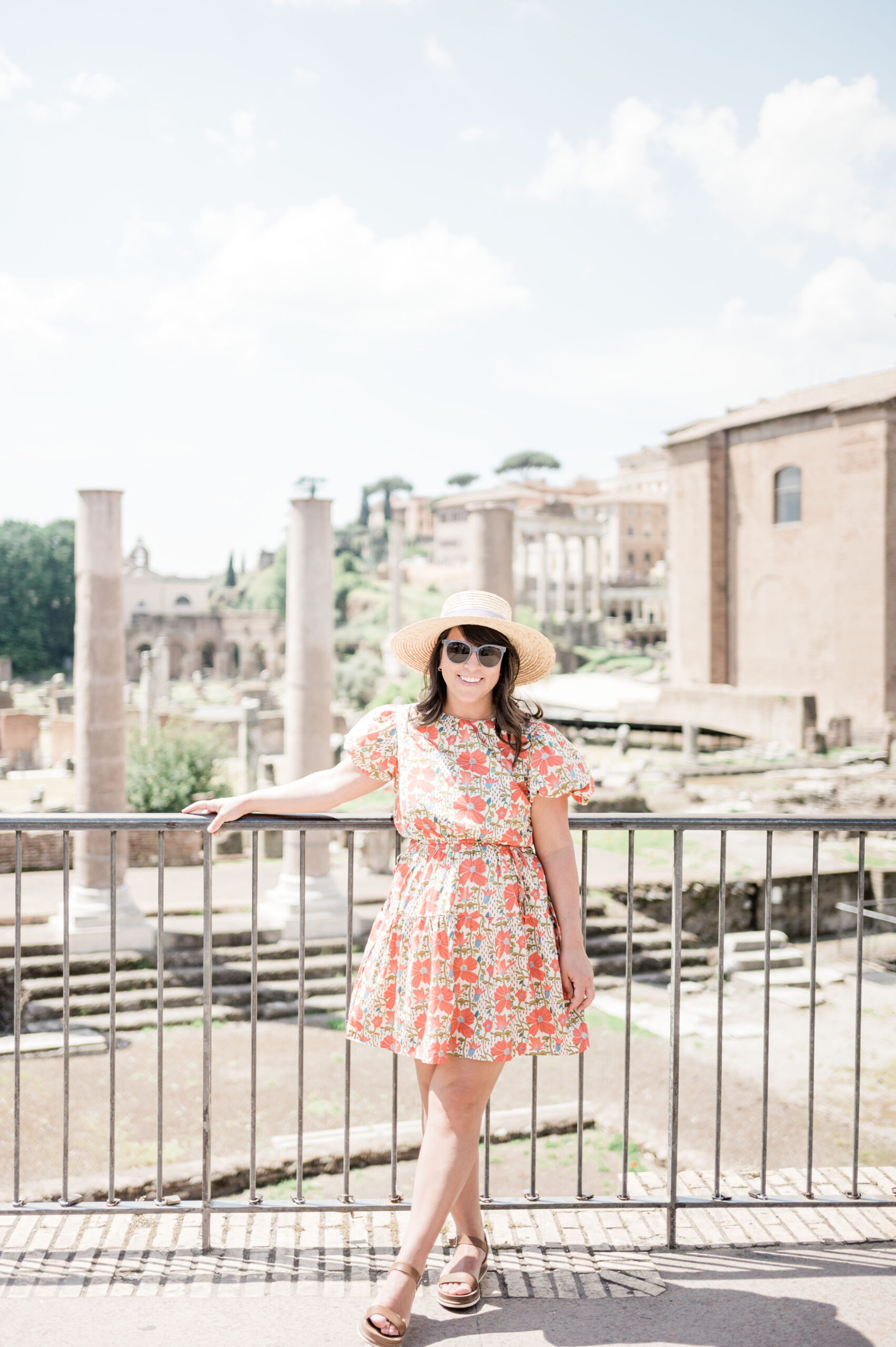 Brittney Naylor standing in front of the Roman Forum. She is wearing a red floral dress, sandals, and sun hat. 36 hours in Rome.