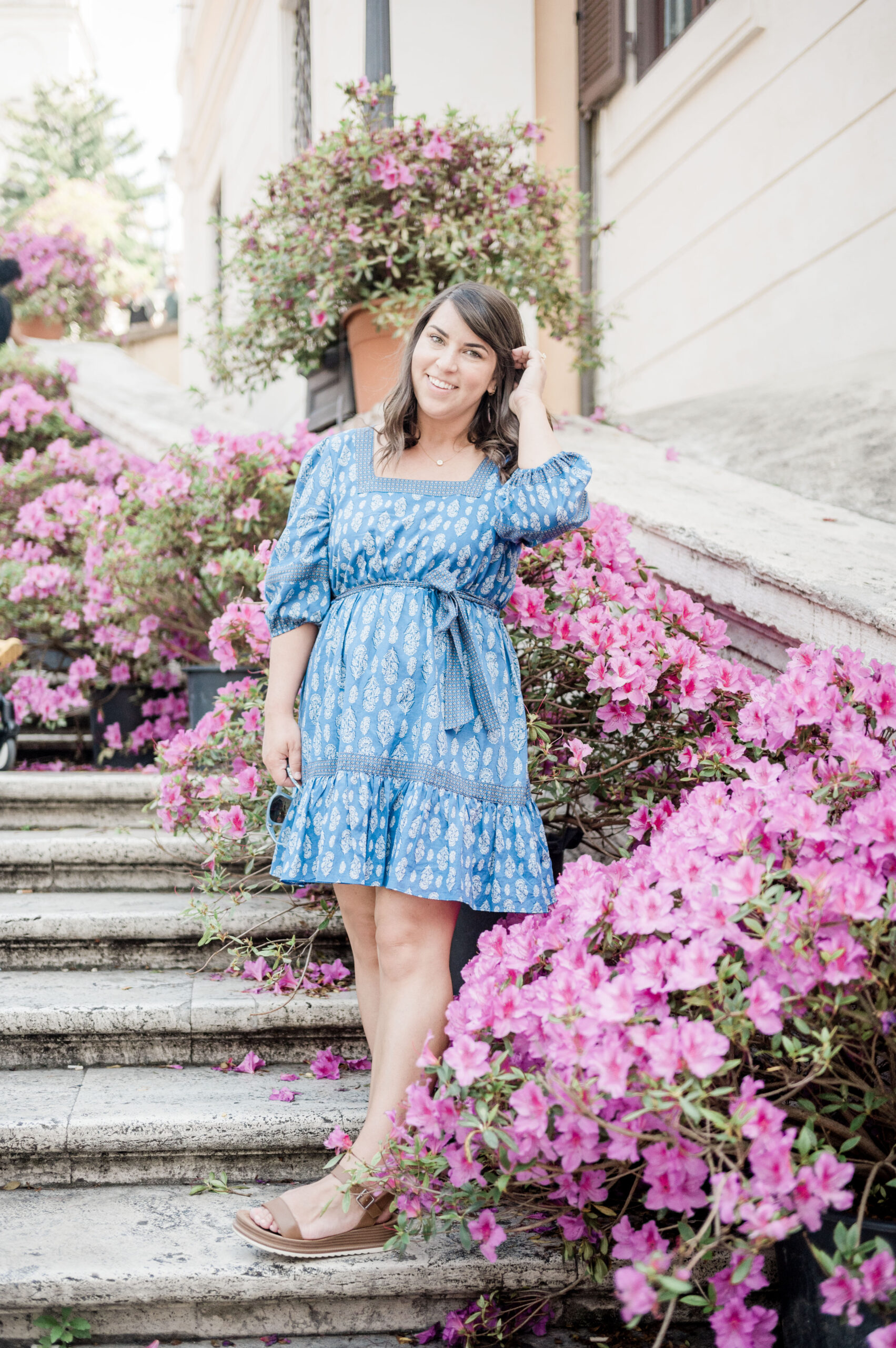 Brittney Naylor in blue knee length dress standing on the Spanish Steps in Rome, Italy surrounded by purple flowers. 36 hours in Rome.