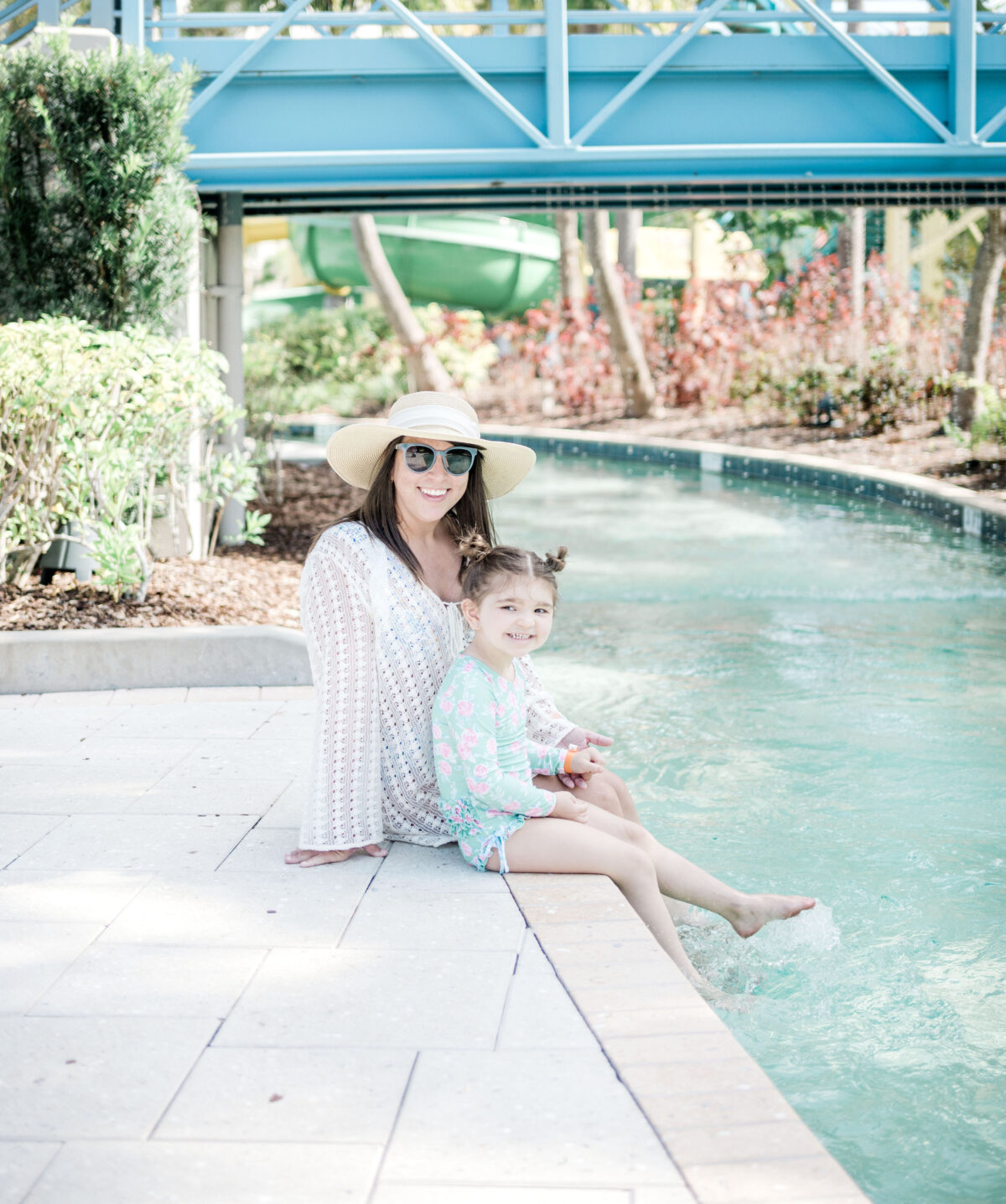 Brittney Naylor and daughter Eleanor sitting on ledge of lazy river at The Grove Resort and Water Park in Orlando. There feet are splashing in the water. Orlando Staycations.