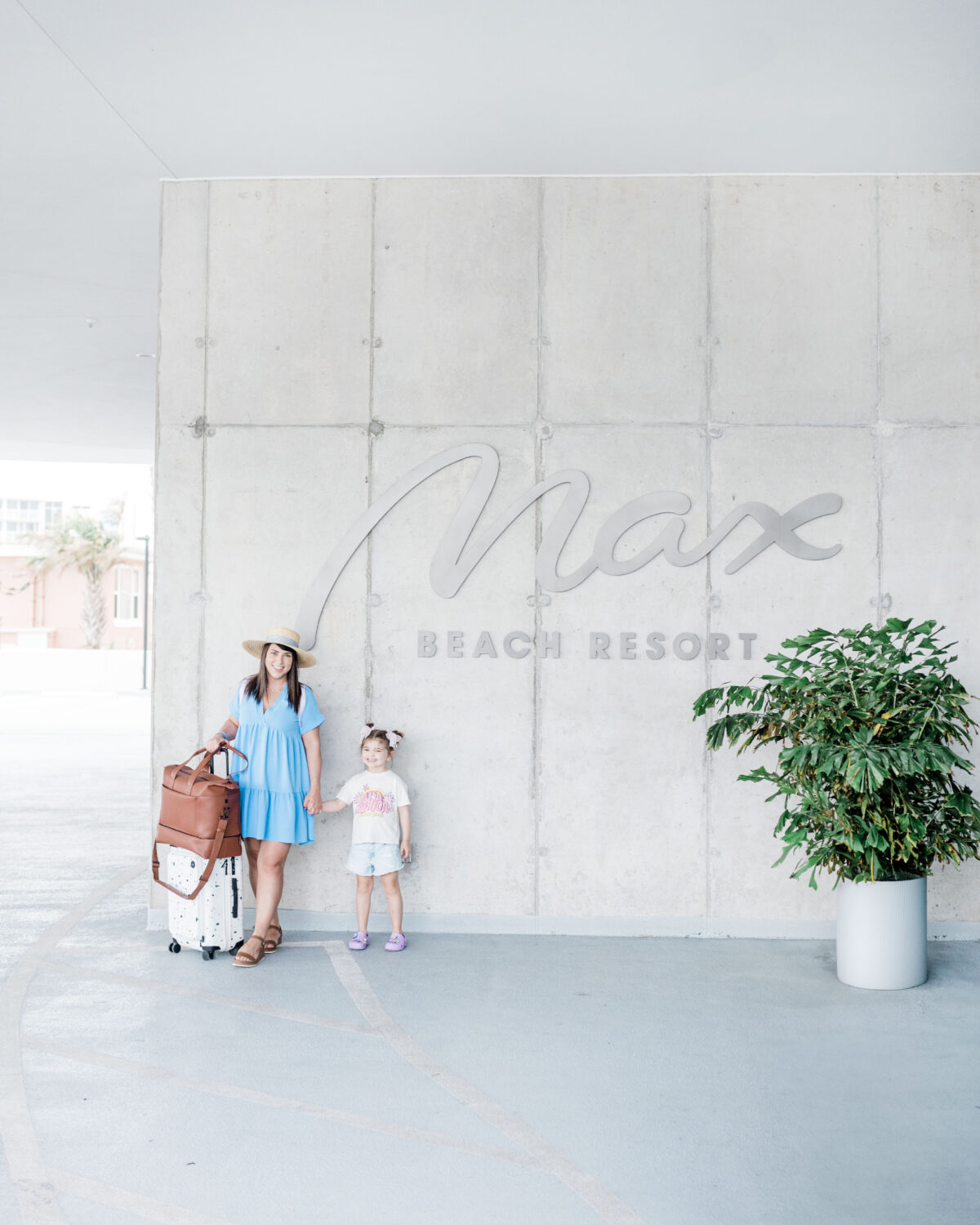 Brittney Naylor and daughter holding hands with luggage beside them standing in front of Max Beach Resort sign, a Daytona Beach Hotel