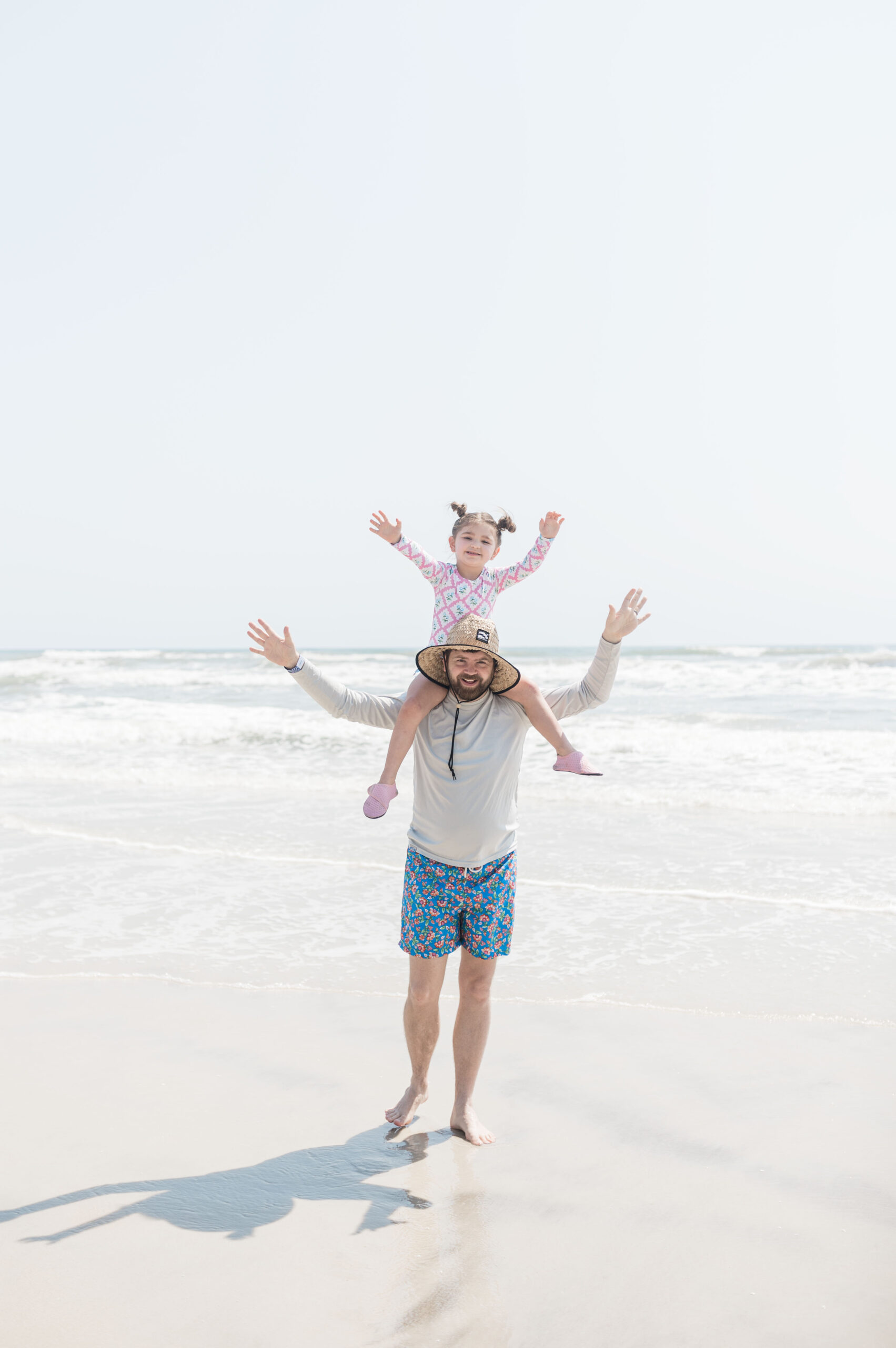 Eleanor on John Naylor's shoulders with their hands out as they walk on the beach in Daytona