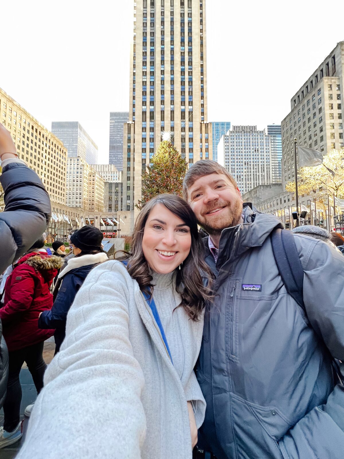 Brittney Naylor and John taking a selfie in front of the Rockefeller Christmas Tree and Plaza. NYC Christmastime Bucket List things to do.