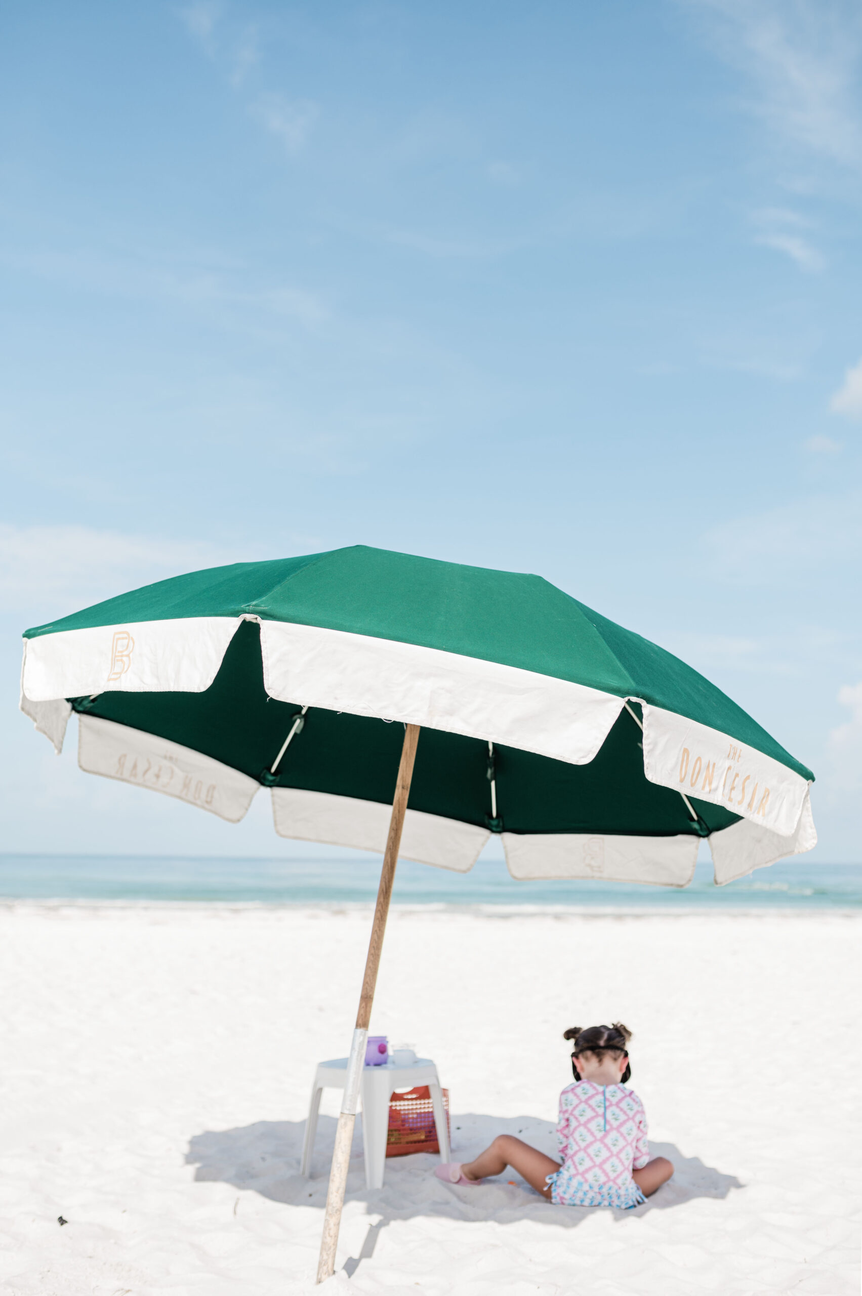 Eleanor playing in the sand under a green beach umbrella that reads The Don CeSar in Saint Pete Beach, Florida, best family resorts in florida