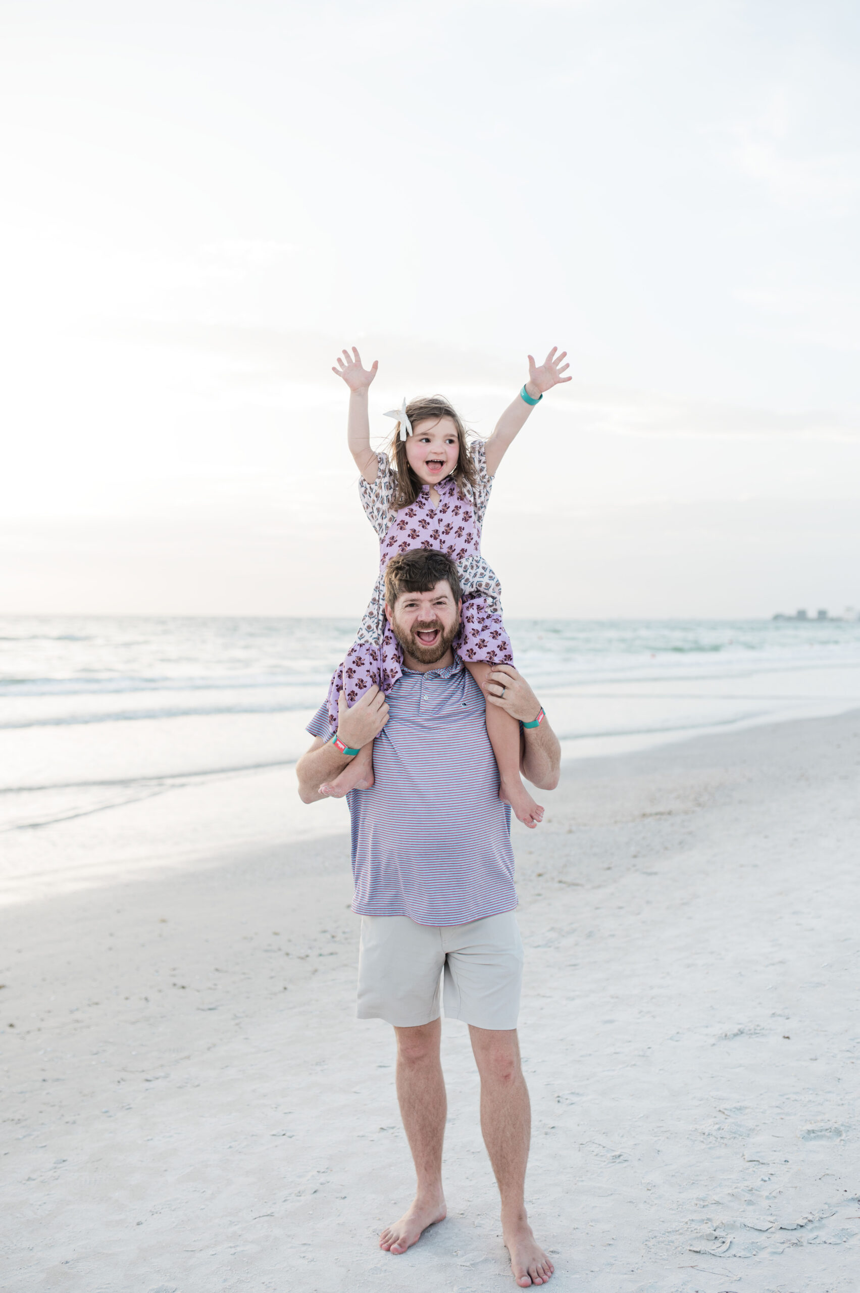 John Naylor and daughter on his shoulders with her hands up on the beach in Saint Pete at the Don Cesar