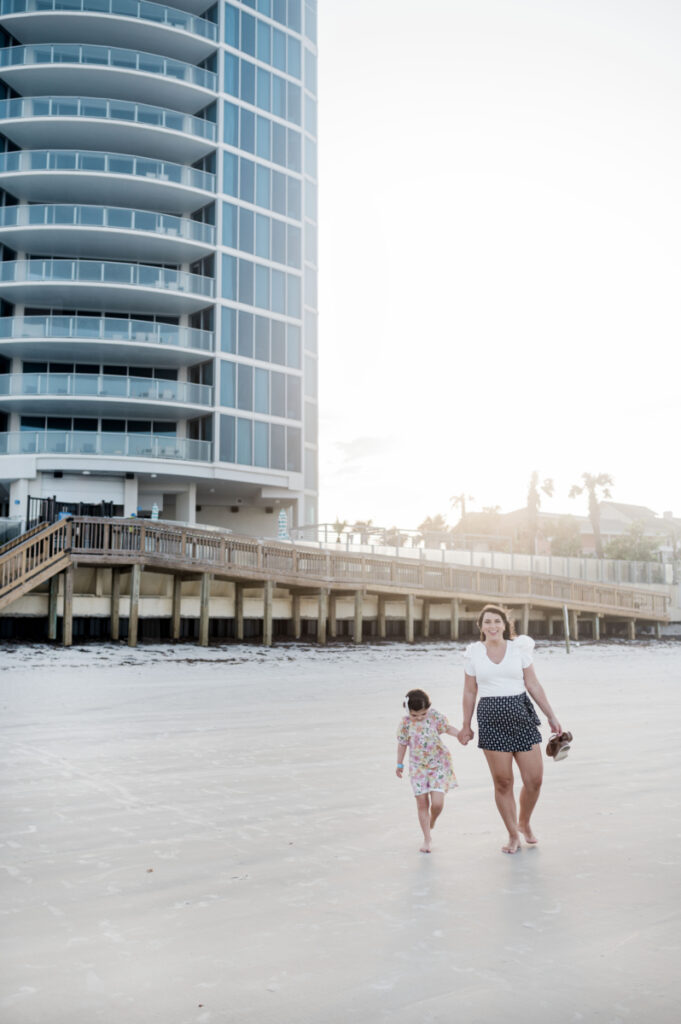 Brittney Naylor holding daughters hand walking on the beach in Daytona with Max Daytona Beach resort in the backgroun. Best Family resorts in Florida