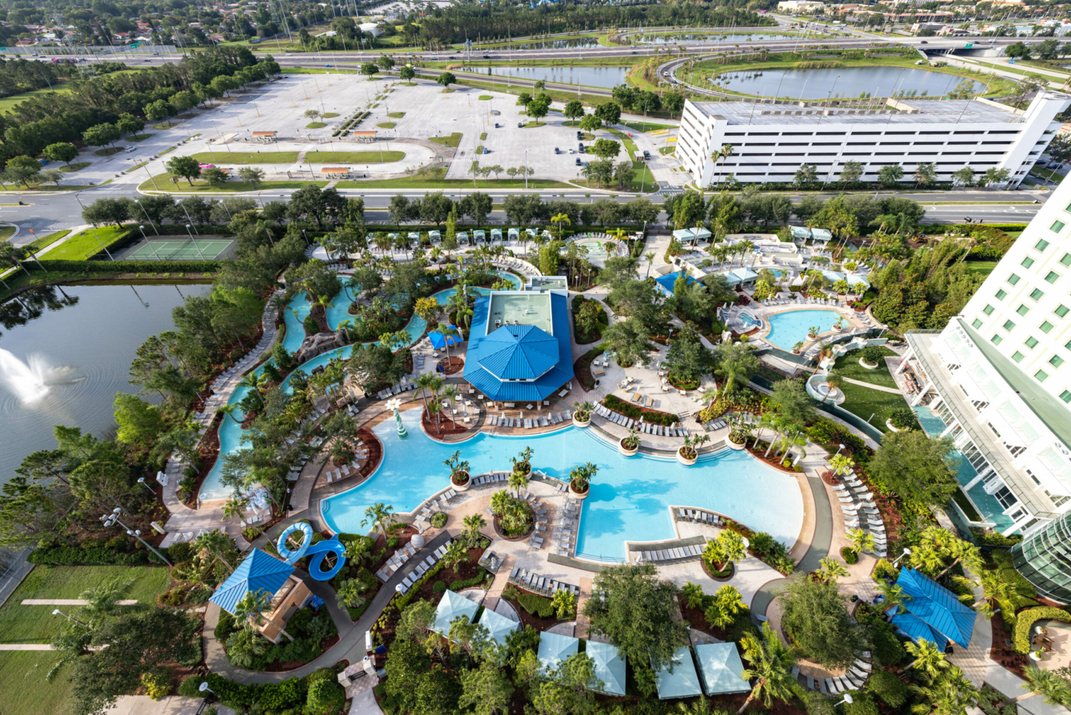 Aerial view of the pool area at hilton orlando featuring a lazy river, blue water slide, and plenty of palm trees. 