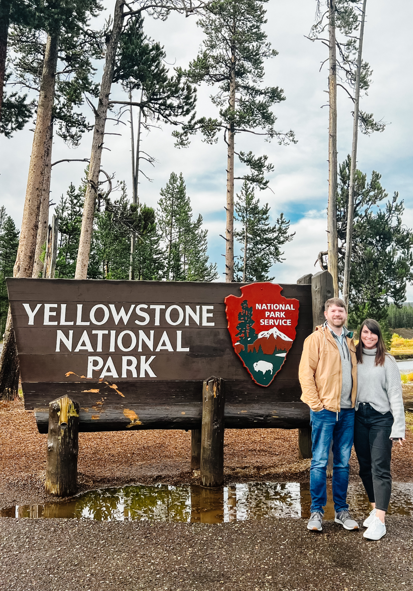 John and Brittney Naylor standing beside the Yellowstone National Park entrance sign--Jackson Hole to Yellowstone tour--everything you need to know