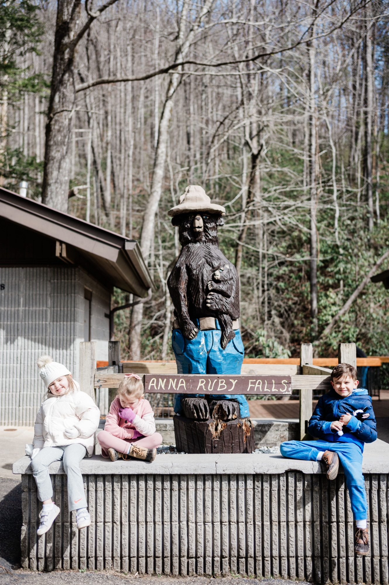 Three kids sitting in front of a statue of Smokey the Bear and a sign saying Anna Ruby Falls--a weekend in Helen, Georgia for families