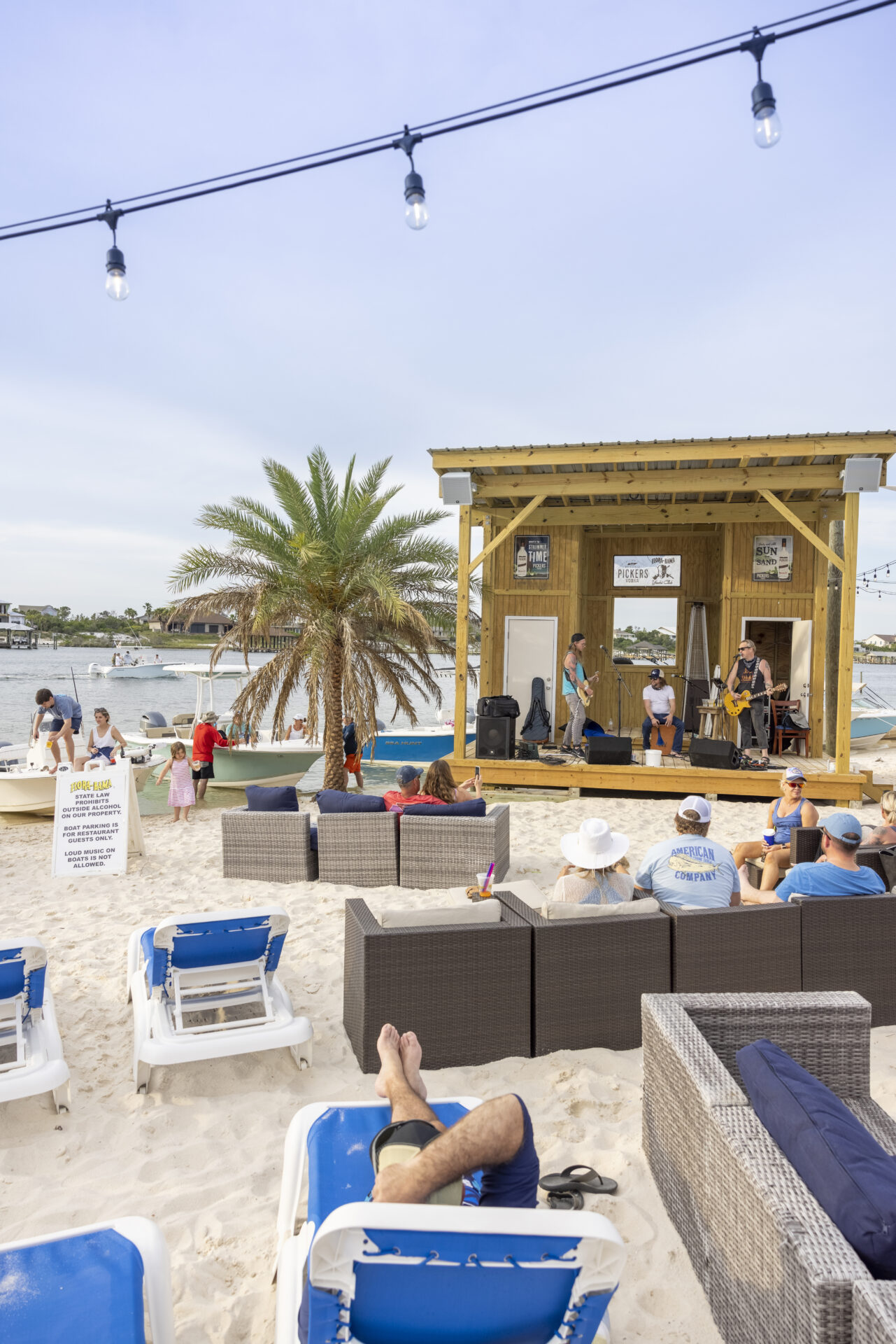 Flora-Bama Yacht Club outdoor space featuring a stage for live entertainment and lounge chairs in the sand. Best family-friendly restaurants in Gulf Shores, Alabama. Photo courtesy of Alabama Beaches Tourism. 