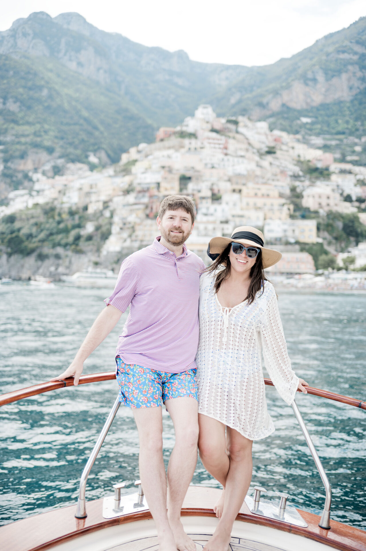 John and Brittney Naylor posing together on a boat in the sea with Positano in the background