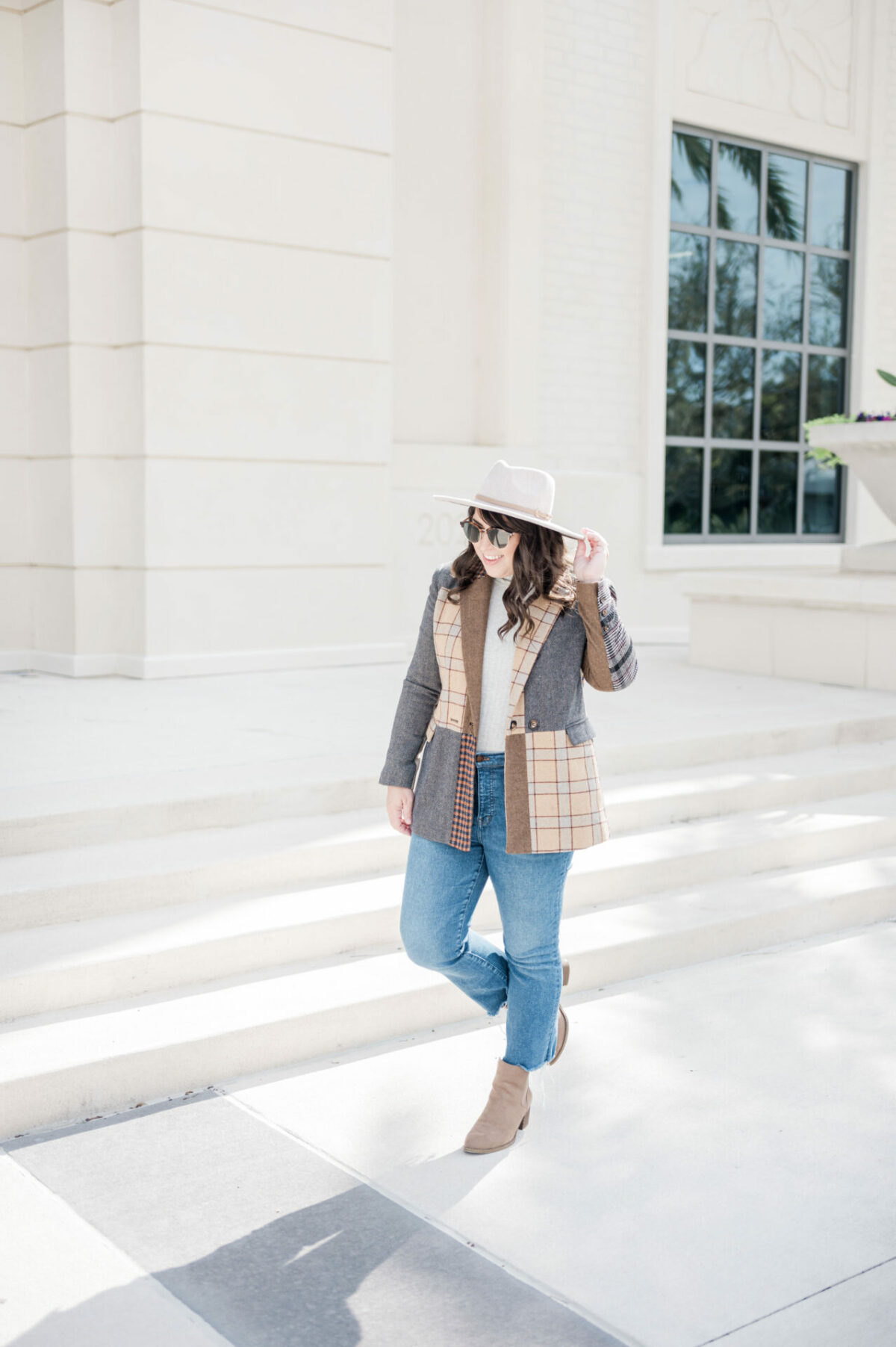 Brittney wearing blazer rented from Rent the Runway, sunglasses rented from Rent the Runway, jeans, and boots walking down sidewalk