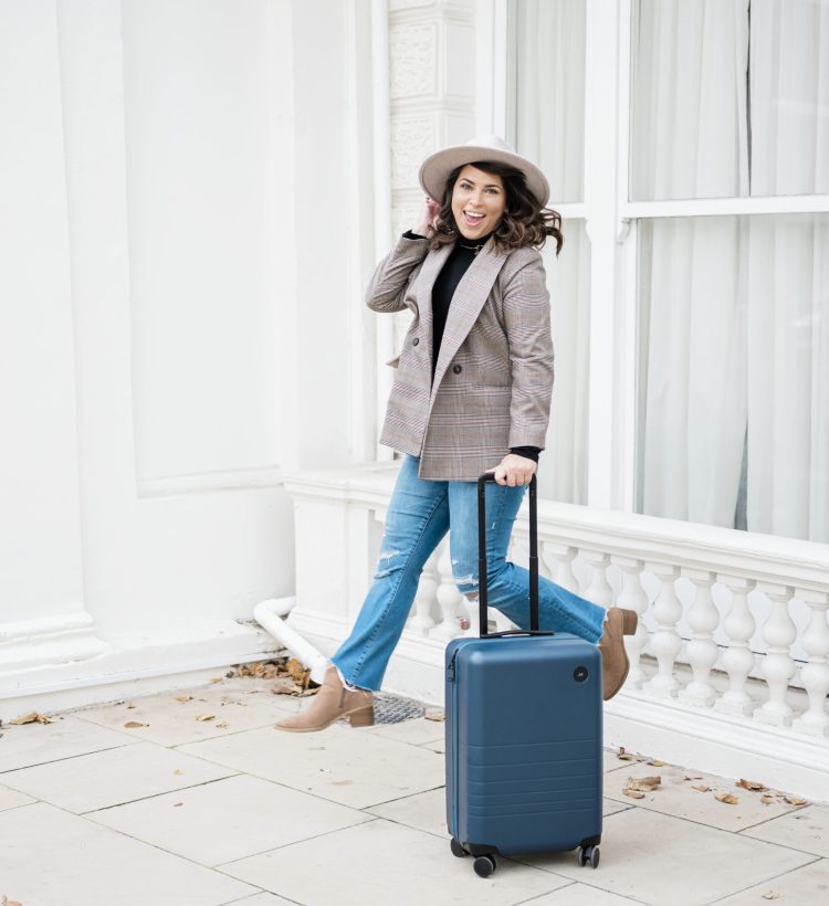 brittney naylor jumping up in the air next to a blue hardshell carryon suitcase